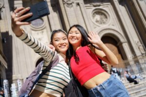 Happy Asian female tourists taking self portrait on smartphone against Cathedral of Granada in Spain