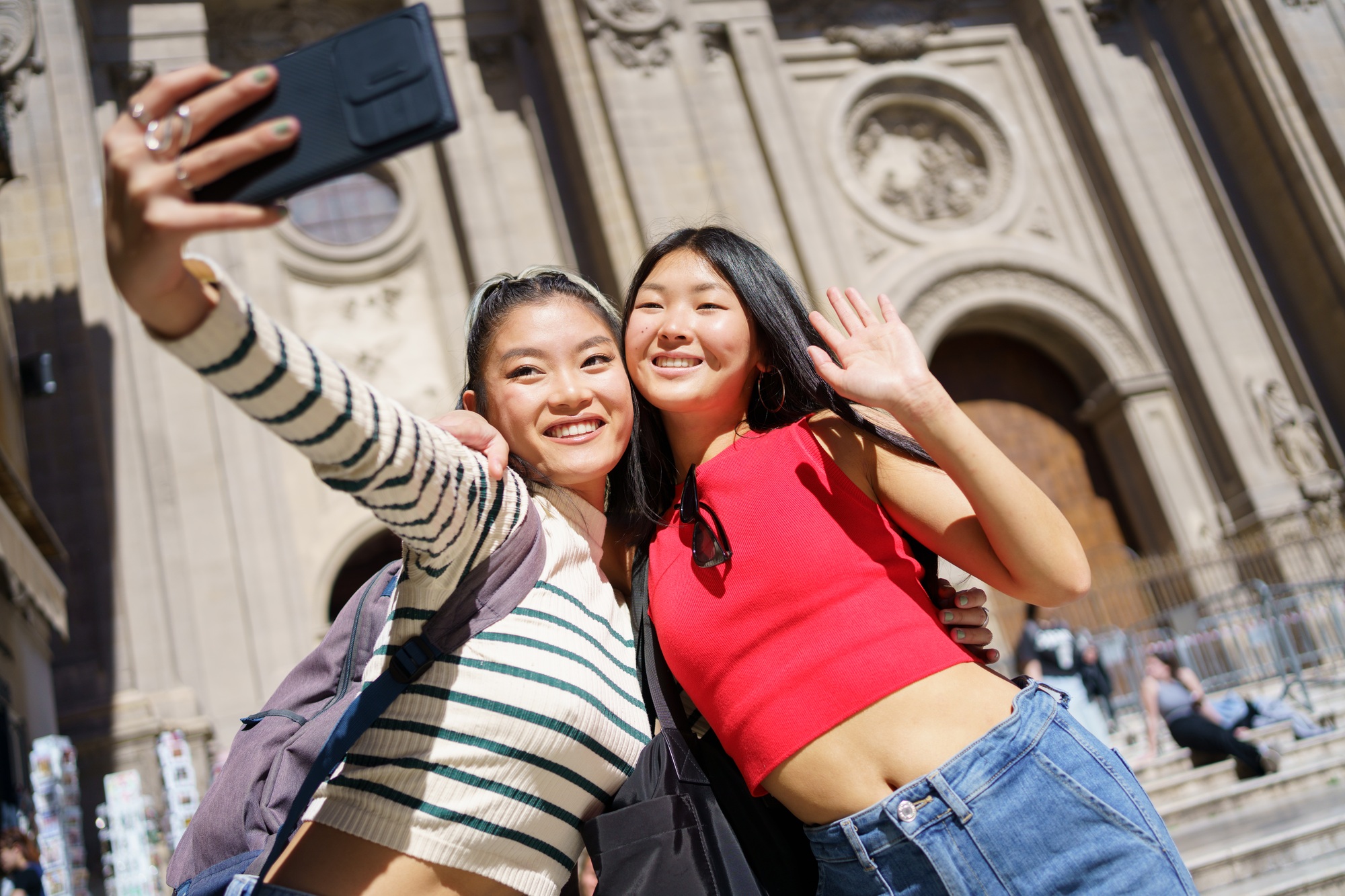 Happy Asian female tourists taking self portrait on smartphone against Cathedral of Granada in Spain