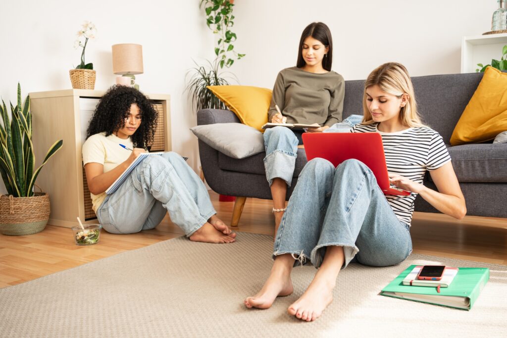 Flatmate student girl friends studying together using laptop to at home