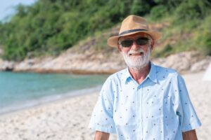 Happy Senior Man at Beach. Elderly man with a straw hat and sunglasses on a sunny beach.