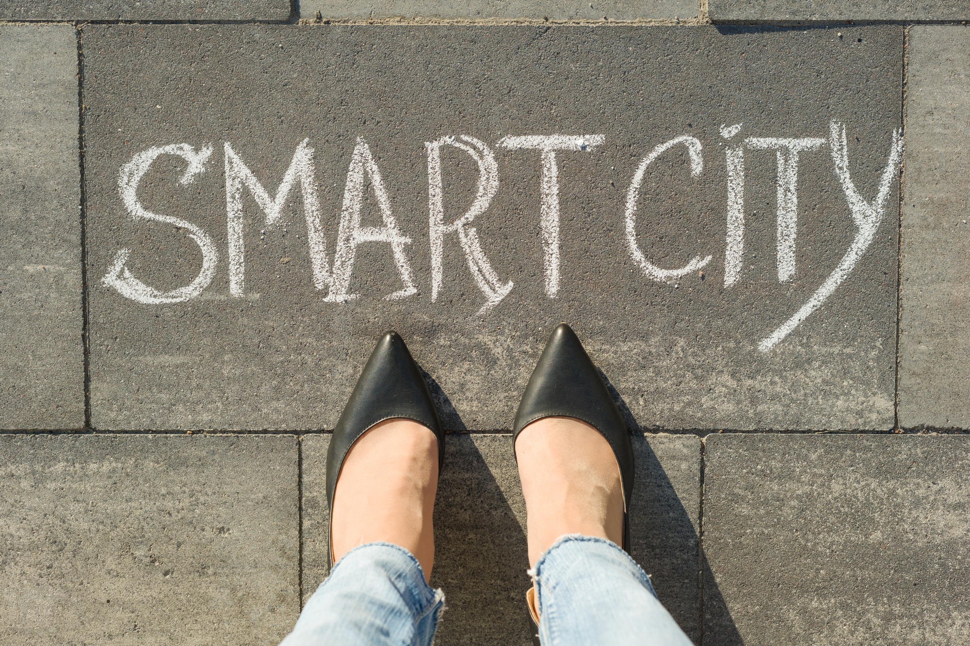 View from above, female feet with text smart city written on grey sidewalk.